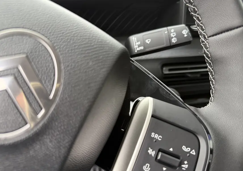 Gros plan sur le volant côté gauche gris noir de la Citroën C3 hybride 2026 avec commandes audio et logo central visible.