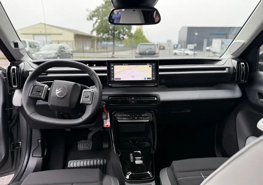 Vue intérieure avant de la Citroën C3 hybride 2026, tableau de bord noir avec écran tactile central et volant multifonction.