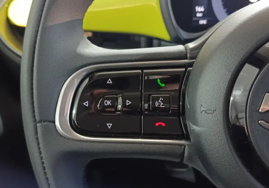 Gros plan sur le volant cuir synthétique noir du Fiat 500 BEV 24KWH 2024 avec commandes multifonctions et tableau de bord jaune visible.