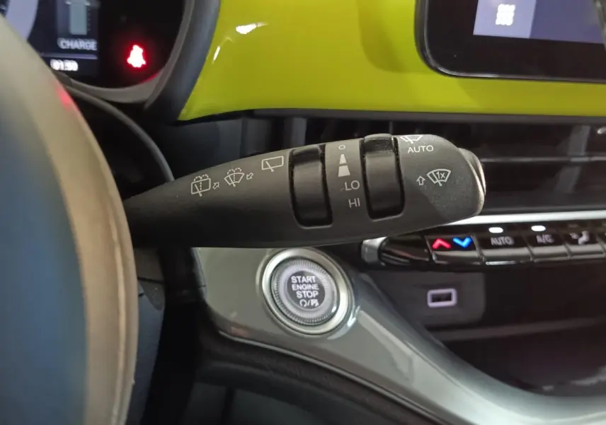 Gros plan sur la commande d’essuie-glace et le bouton start/stop dans l’habitacle jaune vif d’une Fiat 500 électrique 2024.