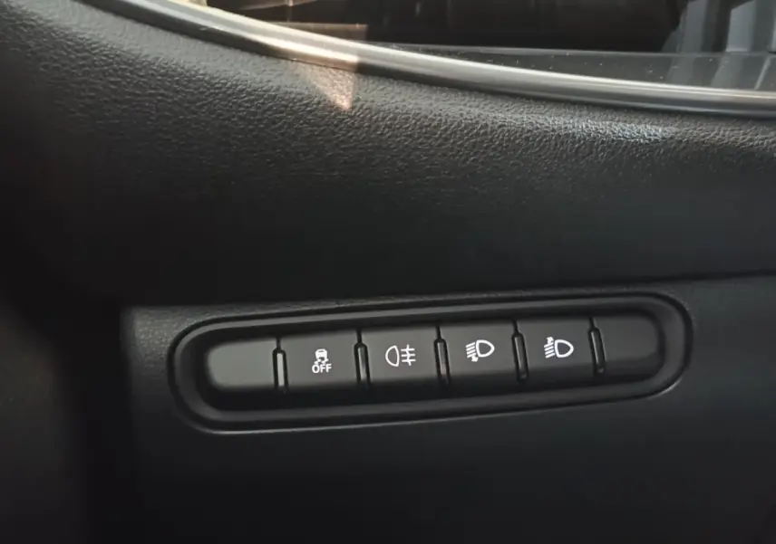 Gros plan sur les boutons de commande des phares et de l'antipatinage dans l'habitacle noir du Fiat 500 BEV 24KWH jaune.