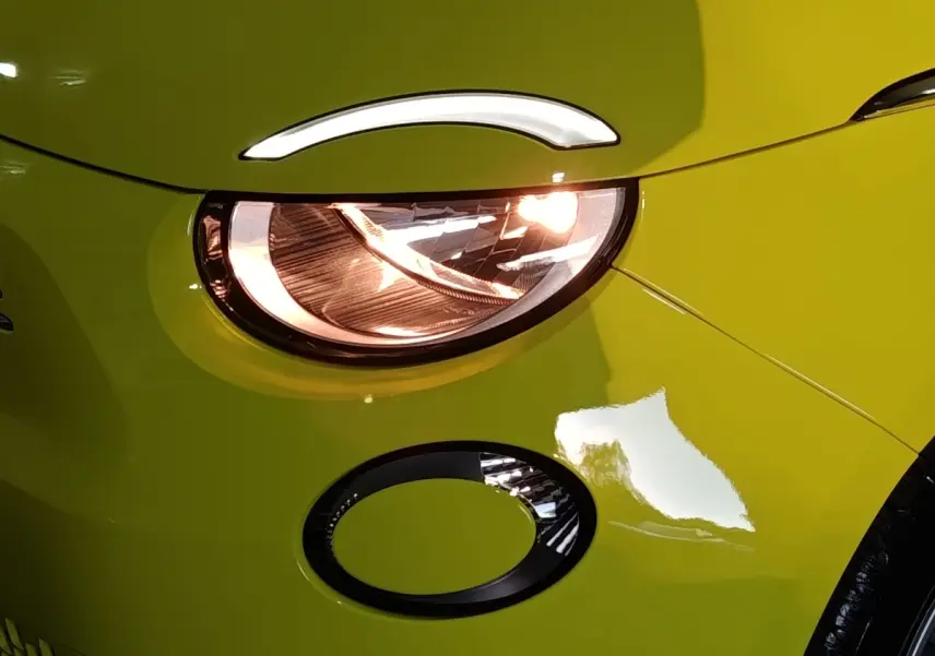 Gros plan sur le phare avant droit allumé d'une FIAT 500 BEV 24KWH jaune vif avec détail du clignotant rond noir.
