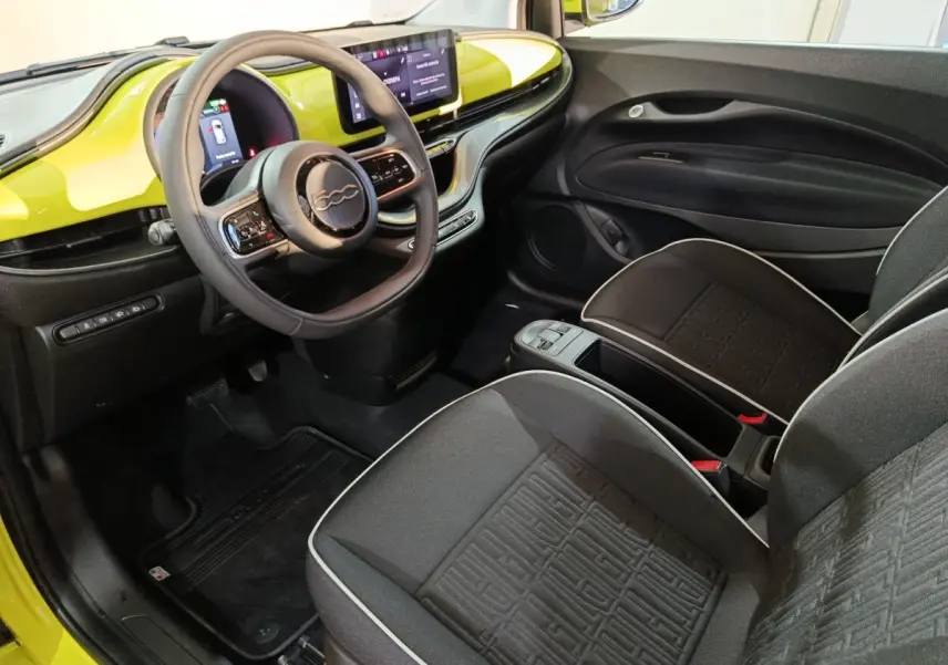 Vue intérieure côté conducteur de la Fiat 500 BEV 24KWH 2024 avec tableau de bord jaune et volant multifonctions cuir synthétique.