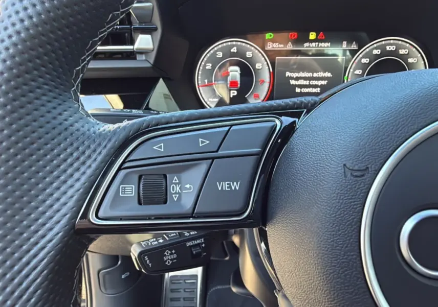 Gros plan sur les commandes gauche du volant cuir perforé de l'Audi A3 TFSI 150 Hybrid S-Line 2025.