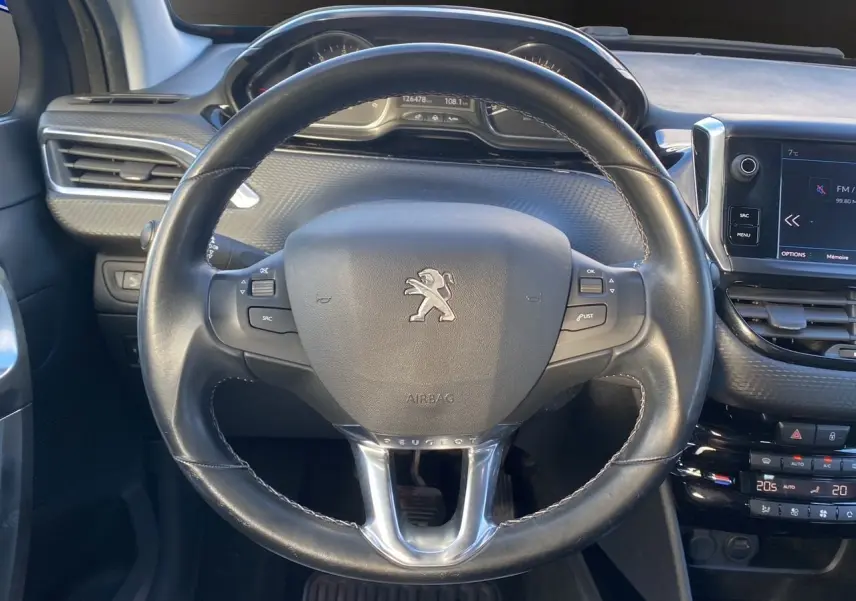 Vue intérieure centrée sur le volant cuir noir du Peugeot 2008 gris platinium avec tableau de bord et écran tactile.