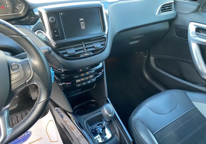 Vue intérieure côté conducteur du tableau de bord et console centrale noire du Peugeot 2008 gris platinium avec écran tactile et boîte automatique.