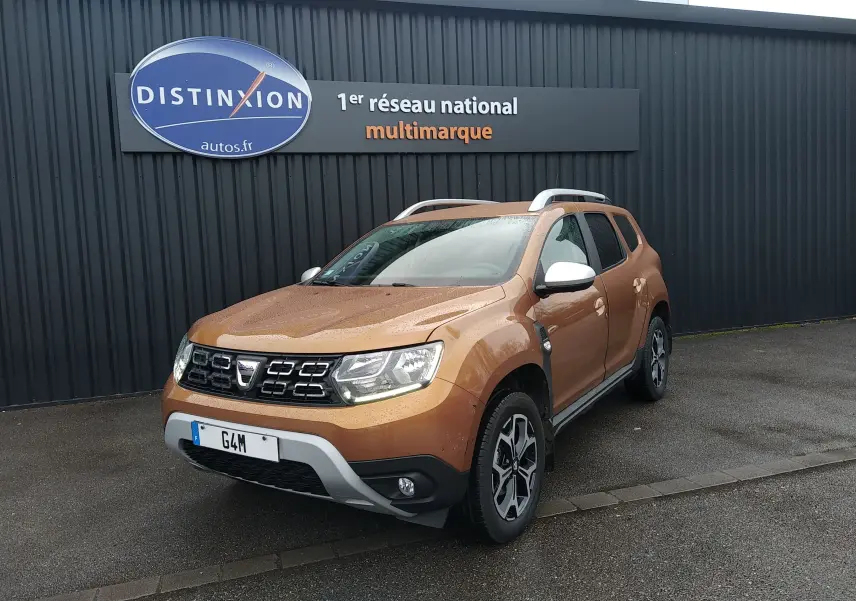 SUV Dacia Duster orange Atacama vu en 3/4 avant droit, avec jantes alliage et barres de toit argentées.