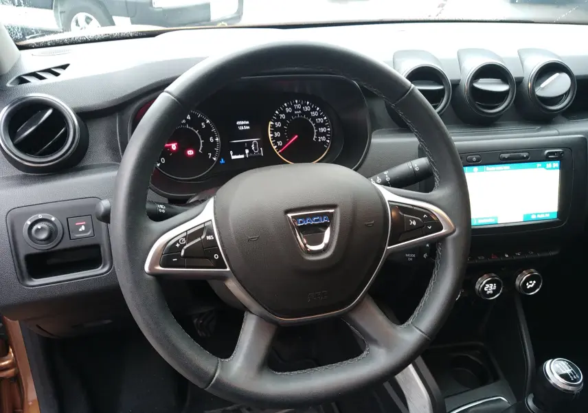 Vue intérieure centrée sur le volant et le tableau de bord du Dacia Duster 2021, avec commandes au volant et écran tactile.