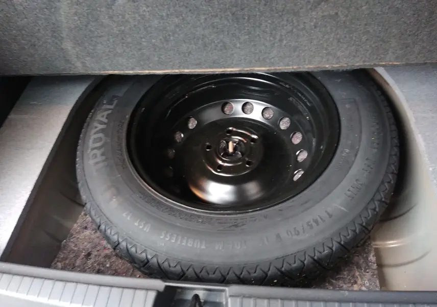 Gros plan sur la roue de secours noire logée dans le coffre d'un Dacia Duster 2021.