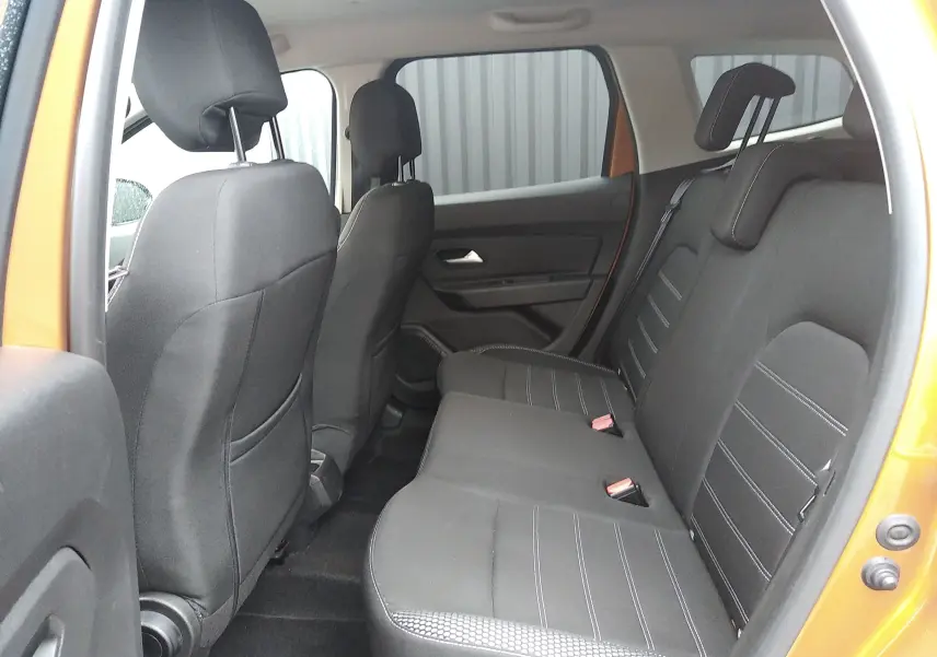 Vue intérieure arrière du Dacia Duster 2021 orange Atacama, montrant les sièges arrière en tissu noir avec surpiqûres grises.