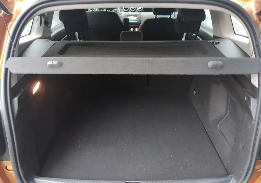 Coffre ouvert vu de l'arrière d'un Dacia Duster orange Atacama 2021, avec tablette cache-bagages et intérieur noir.