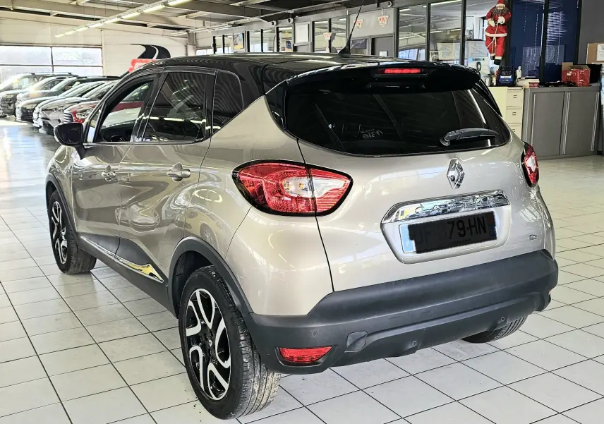 Vue 3/4 arrière droite du Renault Captur gris avec toit noir, jantes alliage et feux arrière allumés en intérieur showroom.