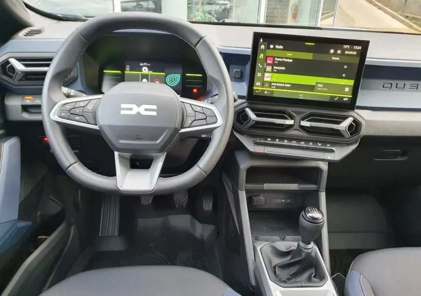 Vue intérieure avant du Dacia Duster 2025 avec volant multifonctions, écran tactile et levier de vitesses manuel.