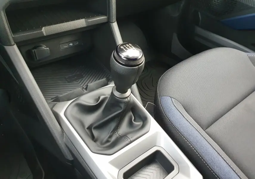 Gros plan intérieur sur le levier de vitesses manuel et la console centrale du Dacia Duster 2025, sièges tissu noir et bleu.