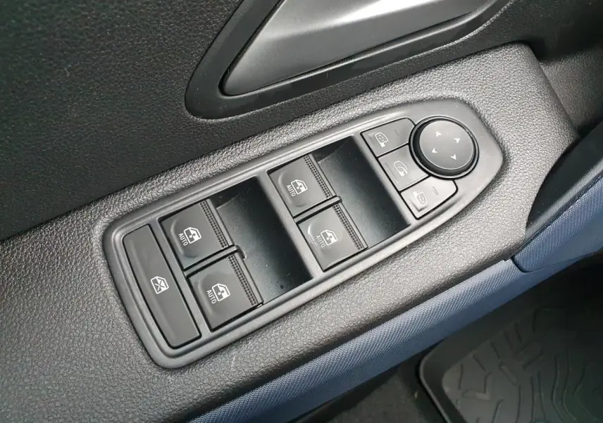 Gros plan sur les commandes de lève-vitres et rétroviseurs côté conducteur du Dacia Duster 2025, intérieur noir et bleu.