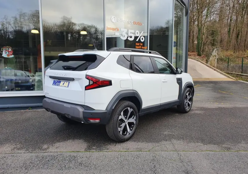 Vue 3/4 arrière droite du Dacia Duster blanc glacier 2025 avec jantes alliage 18” et barres de toit longitudinales.