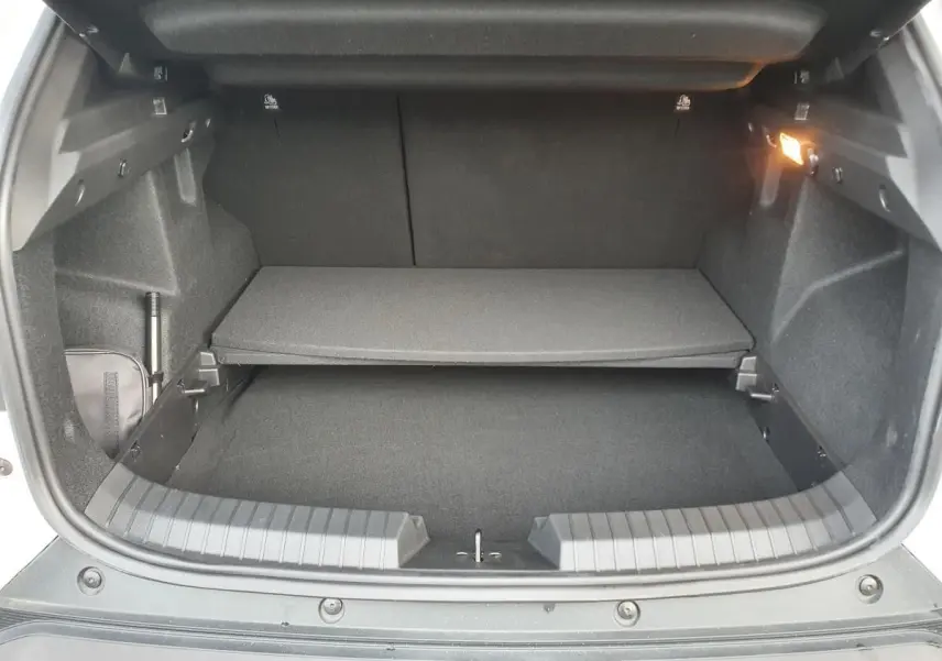 Vue intérieure du coffre du Dacia Duster blanc glacier 2025, avec tablette de rangement et éclairage latéral allumé.