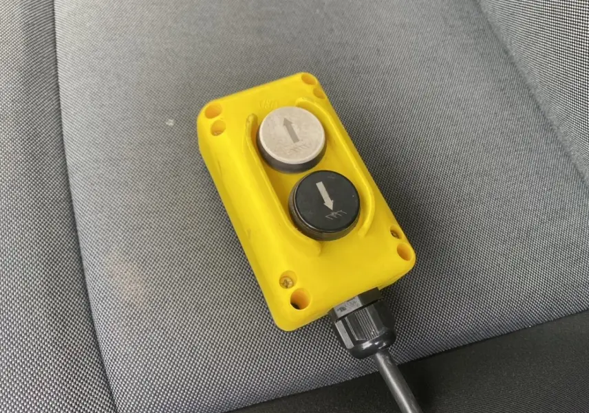 Télécommande jaune avec deux boutons fléchés, posée sur un siège gris à l'intérieur du Renault Master blanc.