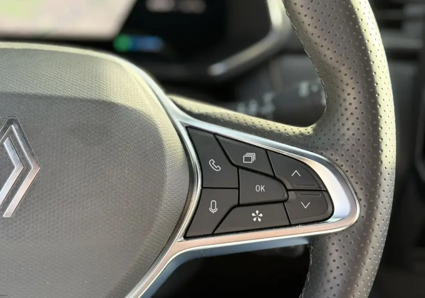 Gros plan sur la partie droite du volant perforé noir du Renault Symbioz gris, avec commandes multifonctions intégrées.