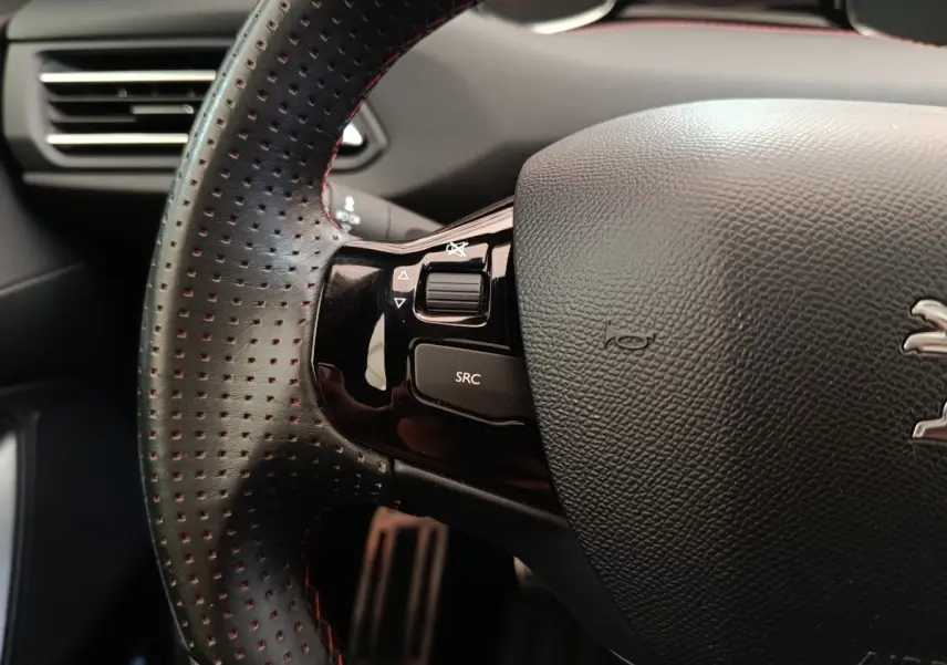 Gros plan sur le volant cuir perforé côté gauche du Peugeot 308 noir, avec commandes multimédia intégrées.