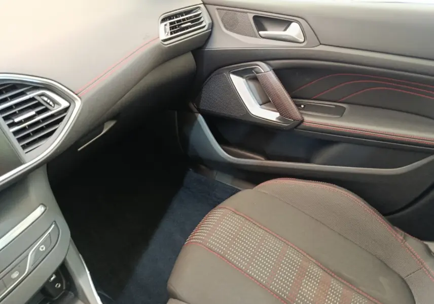 Vue intérieure côté passager avant de la Peugeot 308 GT Line 2016, sièges noirs avec surpiqûres rouges et détails de la portière.