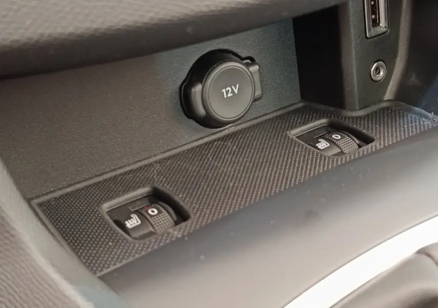 Gros plan sur la console centrale noire de la Peugeot 308, montrant la prise 12V et les commandes de sièges chauffants.