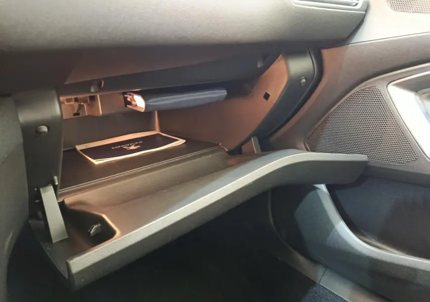 Vue intérieure côté passager de la boîte à gants ouverte de la Peugeot 308 noire, montrant un manuel et un éclairage doux.