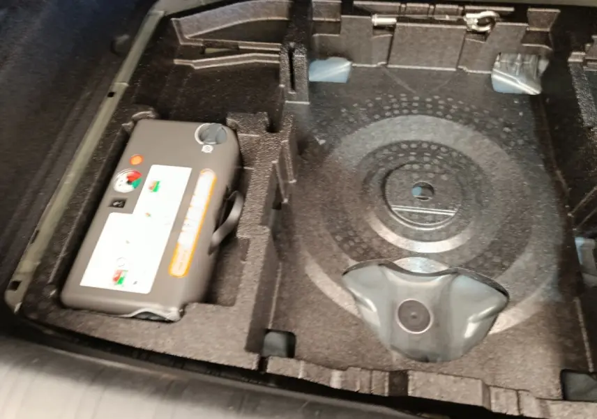 Vue rapprochée du coffre de la Peugeot 308 noir, montrant le rangement sous la tablette avec compresseur et espace pour roue de secours.