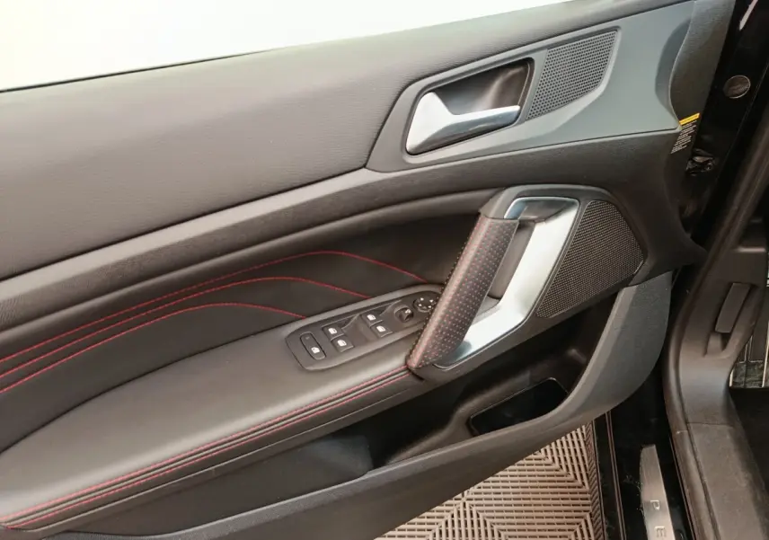 Vue rapprochée de la porte avant gauche noire de la Peugeot 308 GT Line avec surpiqûres rouges et commandes électriques.