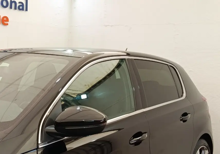 Vue côté gauche avant d'une Peugeot 308 noire 2016 avec rétroviseur ton caisse et vitres teintées.