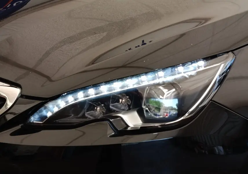 Gros plan sur le phare avant droit LED d'une Peugeot 308 noire, soulignant ses lignes modernes et précises.