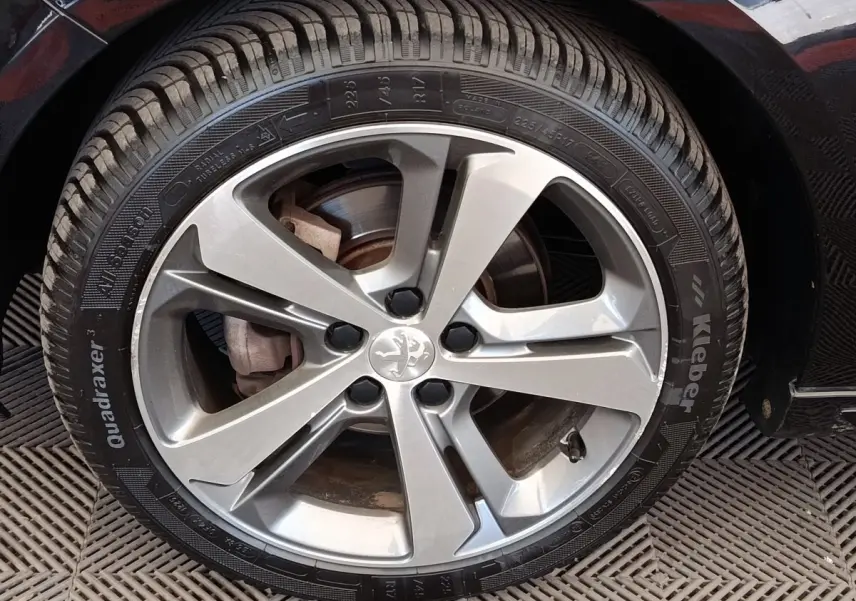 Gros plan sur la roue avant droite d’une Peugeot 308 noire, mettant en valeur la jante alliage et le pneu Kleber.