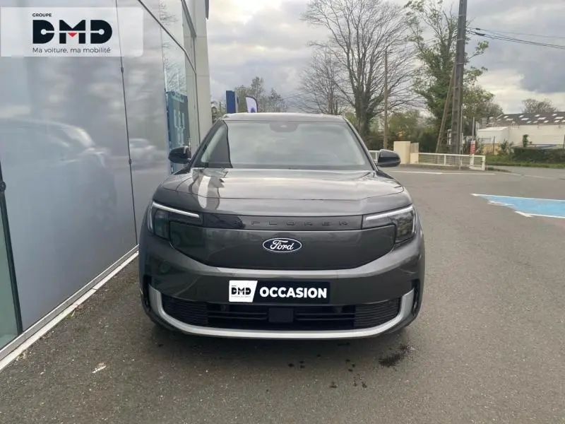 Vue avant d'un Ford Explorer électrique gris Magnetic métallisé avec calandre lisse et logo Ford visible, stationné devant un bâtiment.