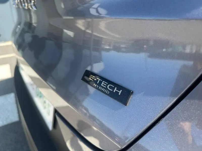Gros plan sur le logo E-TECH Hybrid à l'arrière d'un Renault Captur gris Cassiopée métallisé sous lumière naturelle.