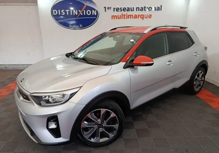 Vue 3/4 avant droit d'un KIA Stonic gris clair avec toit et rétroviseurs orange, roues alliage et barres de toit chromées.