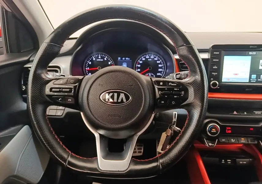 Vue centrée sur le volant cuir noir avec surpiqûres rouges du Kia Stonic gris clair, tableau de bord et écran tactile visibles.