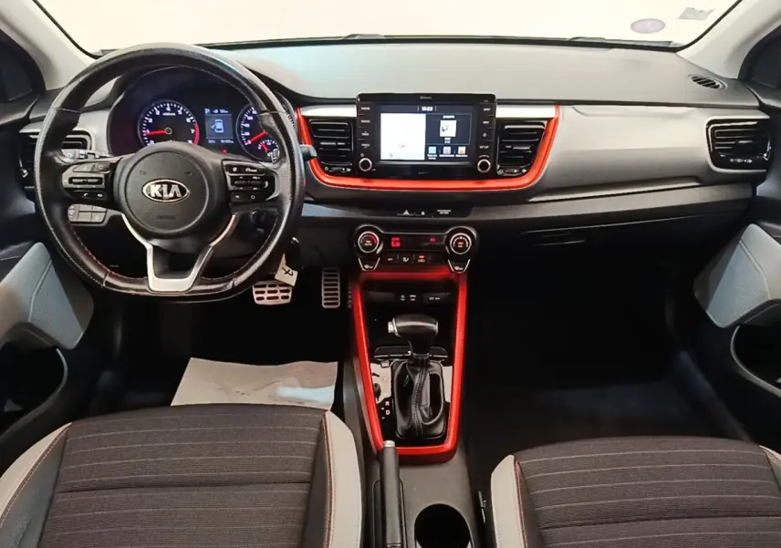Vue intérieure frontale du tableau de bord et volant KIA Stonic 2019, avec insert rouge autour de l'écran tactile et levier de vitesses.