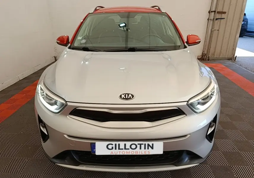 Vue avant frontale du KIA Stonic gris clair avec toit et rétroviseurs rouges, phares allumés en intérieur.