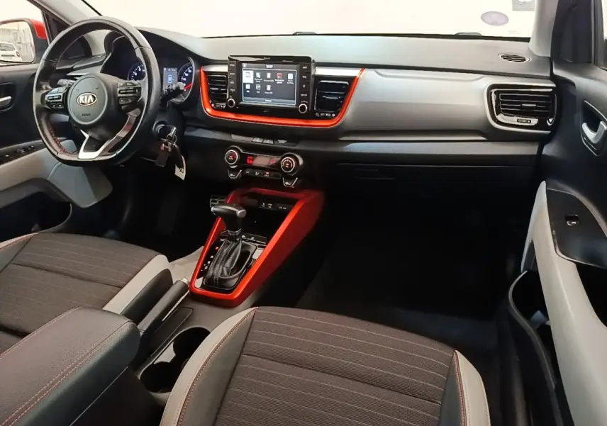 Vue intérieure avant droite du Kia Stonic 2019, tableau de bord gris clair avec inserts orange et écran tactile central.