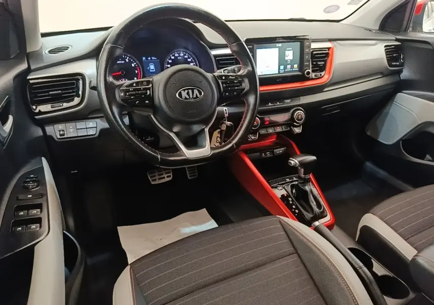 Intérieur avant du Kia Stonic gris clair, vue centrée sur le volant multifonctions et la console tactile rouge.