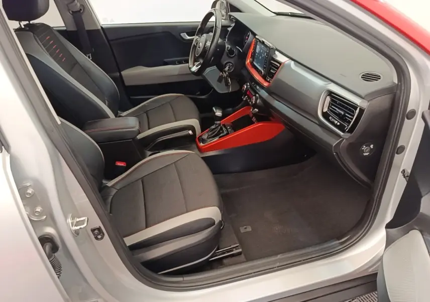 Vue intérieure côté conducteur d'un KIA Stonic gris clair 2019 avec sellerie noire et inserts rouges autour de la console centrale.