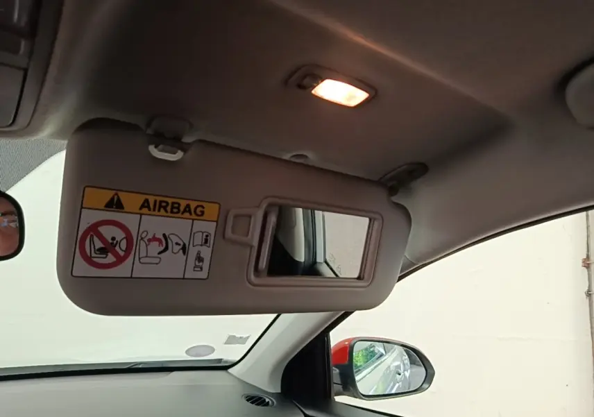 Vue intérieure du pare-soleil côté conducteur avec miroir et lumière, rétroviseur extérieur visible sur fond clair.