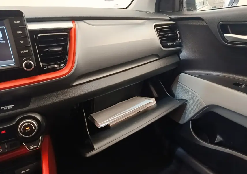 Intérieur KIA Stonic 2019 vu côté passager, tableau de bord gris clair avec encadrement orange et boîte à gants ouverte.