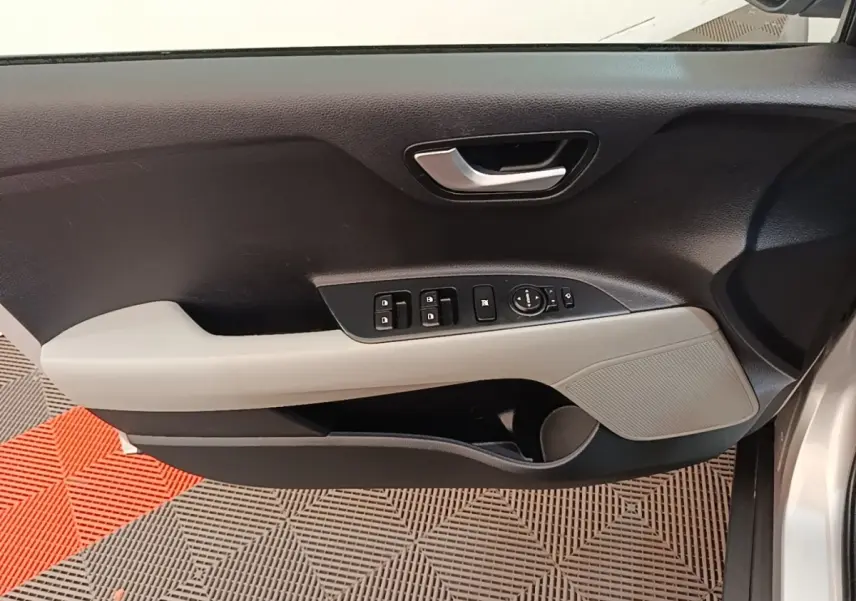 Vue intérieure côté conducteur de la porte d’une KIA Stonic gris clair avec commandes électriques et poignée argentée.