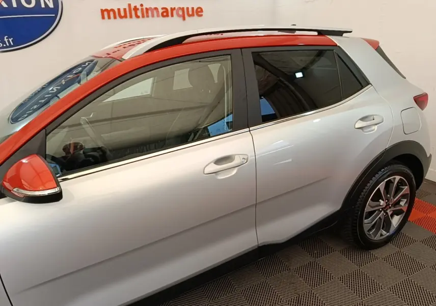 KIA Stonic gris clair vue de profil côté gauche, toit et rétroviseur orange, jantes alliage et rails de toit chromés.