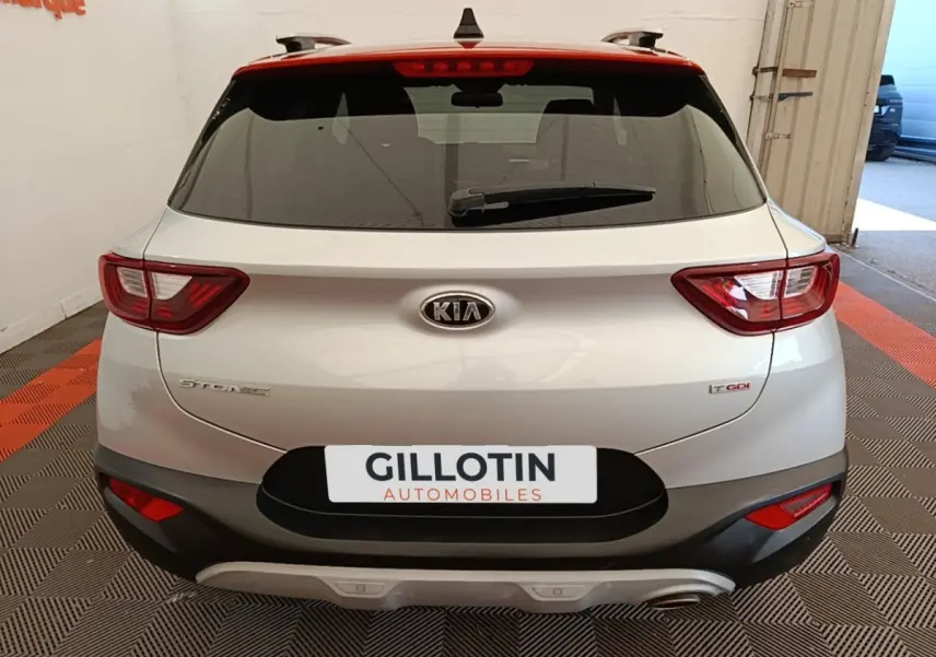 Vue arrière d'un KIA Stonic gris clair avec feux LED et logo visible, stationné en intérieur sur sol à damier.