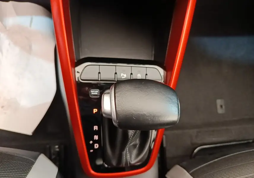 Le levier de vitesses automatique noir encadré d'un contour rouge dans l'habitacle d'une KIA STONIC gris clair.