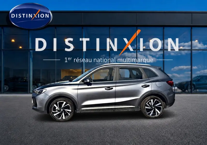 Vue latérale droite du MG Motor ZS gris 2026 avec jantes alliage noires et toit surélevé devant une vitrine Distinxion.