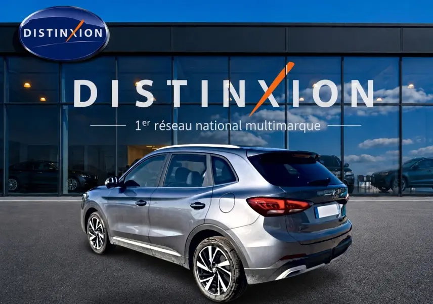MG Motor ZS gris en 3/4 arrière droit, avec jantes alliage et feux arrière LED visibles devant un showroom Distinxion.