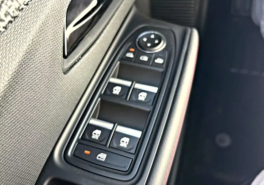 Gros plan sur la commande des vitres électriques côté gauche d’une Renault Clio VI noire, avec surpiqûres rouges.
